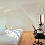 Schlafzimmer mit Dachschräge, Bett, Schreibtisch und Fenster.