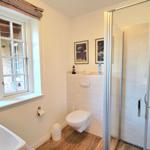 Badezimmer mit Dusche, Toilette und Fenster. Holzfußboden und weiße Wände.