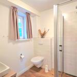 Badezimmer mit Dusche, WC und Waschbecken. Fenster mit Vorhängen.