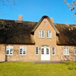 Haus mit strohgedecktem Dach und rotem Backsteinbau. Weiße Fenster und Tür. Grasfläche vor dem Haus.