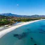 Beach with clear water, sand, and green landscape in the background.