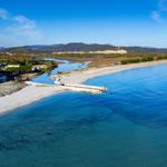 Beach with clear water, river, and hills in the background.