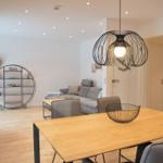 Essbereich mit Holztisch und Stühlen. Wohnbereich mit Sofa und runden Regal.