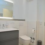 Badezimmer mit Waschbecken, Spiegel und Toilette. Blick in angrenzenden Raum.