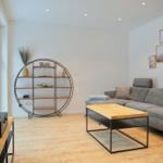 Wohnzimmer mit grauem Sofa, Holztisch und runden Regal.