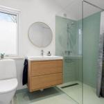 Bathroom with shower, sink, and toilet. Green tiles and wooden vanity.
