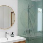 Bathroom with shower, sink, and round mirror.