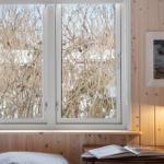 A window with a view of bare branches, beside a lamp and an open book.