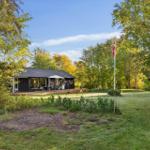 A modern house with a terrace, surrounded by grass and trees. A Danish flag flies.