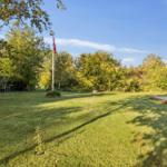 Large garden with terrace, table, chairs, and flag. Surrounded by trees and shrubs.