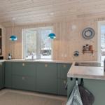 Kitchen with green cabinets, wooden walls, and windows to snow