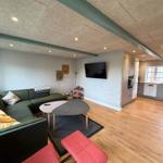 Living area with sofa, table, and TV. Kitchen with countertop and window.