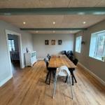 Dining room with wooden floor, long table and chairs. Windows and door visible.