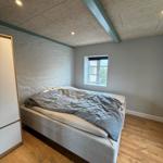 Bedroom with bed, wooden floor, and window. Ceiling with beams.