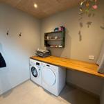 Laundry room with washing machine and dryer, wooden counter and wall shelf.