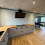 Kitchen with wooden surfaces and white wall. Dining area with table and chairs in background.