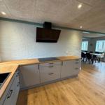Kitchen with wooden countertop and white cabinets. Dining area with table and chairs in background.