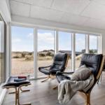 Zwei schwarze Ledersessel mit Holzrahmen stehen vor großen Fenstern mit Strandblick.