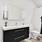 Badezimmer mit Waschtisch, Spiegel und Toilette. Schwarzer Schrank und schwarzes Handtuch.