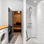 Dusche mit Duschbrause, Waschmaschine und Sauna im Hintergrund.