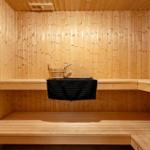 Sauna mit Holzbank und Eimer. Schwarze Handtücher hängen auf der Bank.