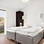 Schlafzimmer mit Doppelbett, dunklen Schränken und Blick auf Dünensand.