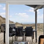 Terrasse mit Tisch und Stühlen, Blick auf Strand und Dünen.