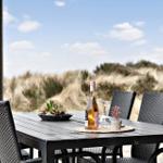 Terrasse mit Tisch und Stühlen, Blick auf Dünen und Himmel.