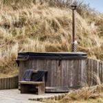 Holzwhirlpool mit Sitzbank und Schornstein auf Holzterrasse vor Grasberge