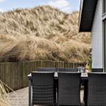 Terrasse mit Tisch und Stühlen neben einem Haus mit Dünen im Hintergrund.