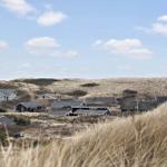 Dorf zwischen Dünen mit Häusern unter blauem Himmel.