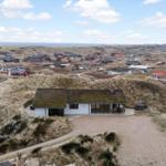 Moderne Villa mit Grasdach auf Dünen, Blick auf Küstenlandschaft mit Häusern.