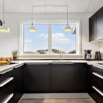 Küche mit dunklen Schränken, Arbeitsfläche und Fenster mit Blick auf Dünen.