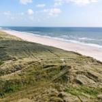 Weitläufiger Strand mit Dünen und Meer unter blauem Himmel.
