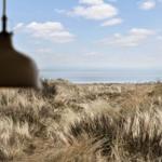 Durch das Fenster sieht man das Meer und trockenes Gras.