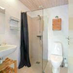 Badezimmer mit Dusche, Toilette und Waschbecken auf Holzgestell.