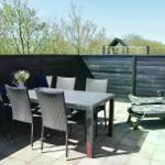 Terrasse mit Tisch, Stühlen und Liegestühlen. Hintergrund: Holzzaun und Bäume.