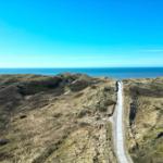 Hügelige Landschaft mit Blick auf das Meer und einem Weg zum Strand.