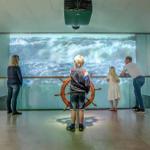 Besucher betrachten eine maritime Projektion mit Ruder und Skulpturen an den Wänden.