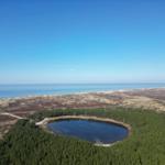 Ein See liegt inmitten eines Waldes, umgeben von Hügeln und dem Meer.