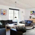 Wohnzimmer mit schwarzen Sofas, weißem Tisch und bunten Bildern an den Wänden.