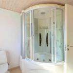 Bad mit Dusche und Toilette. Holzdecke und weißer Fliesenboden.