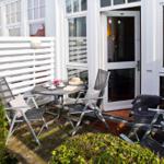 Terrasse mit Tisch, Stühlen und Pflanzen vor weißem Haus