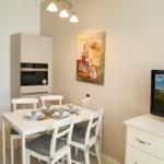 Esszimmer mit Tisch, Stühlen und integriertem Ofen. Fernseher zeigt Strandbild.