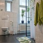 Badezimmer mit Toilette, Waschbecken und Dusche. Grüne Handtücher und Pflanzen im Fenster.