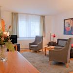 Wohnzimmer mit Sofa, Sessel, Couchtisch und Fenster mit Vorhängen.
