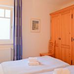 Schlafzimmer mit Doppelbett, Holzschrank und Fenster mit Vorhängen.