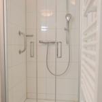 Dusche mit Handbrause, Haltegriff und Heizkörper an der Wand.