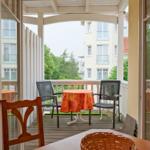 Terrasse mit Tisch, zwei Stühlen und orangefarbener Tischdecke.