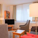 Wohnzimmer mit Sofa, Sessel, Fernseher und Tisch.